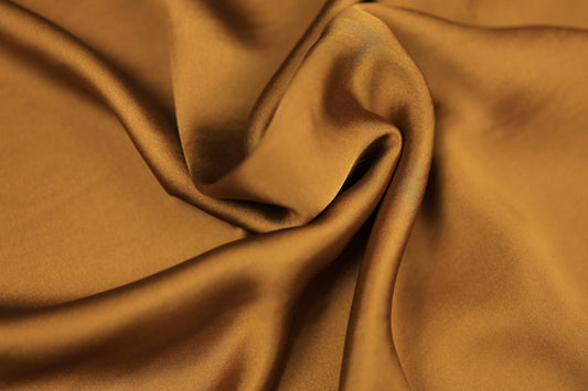 Detailaufnahme von karamellbraunem Satinstoff mit sanftem Faltenwurf und seidig glänzender Oberfläche