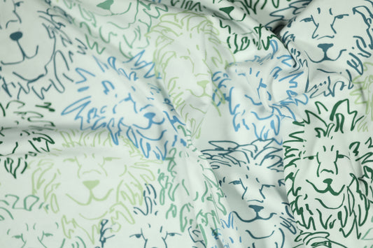 Weißer Kinderstoff mit einem Muster aus gezeichneten Löwenköpfen in Grün und Blau