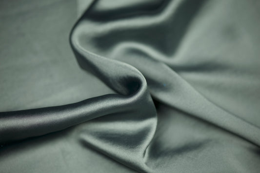 Nahaufnahme eines luxuriösen Satinstoffs in elegantem Salbeigrün mit sanftem Schimmer und natürlichem Faltenwurf – ideal für dezente Mode und Wohntextilien.