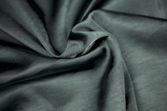 Nahaufnahme eines luxuriösen Satinstoffs in dunklem Schiefergrau mit elegantem Glanz und natürlichem Faltenwurf – ideal für stilvolle Nähprojekte