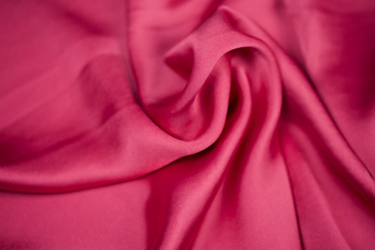 Nahaufnahme eines luxuriösen Satinstoffs in intensivem Himbeerrosa mit elegantem Glanz und dekorativer Faltenstruktur – ideal für auffällige Nähprojekte
