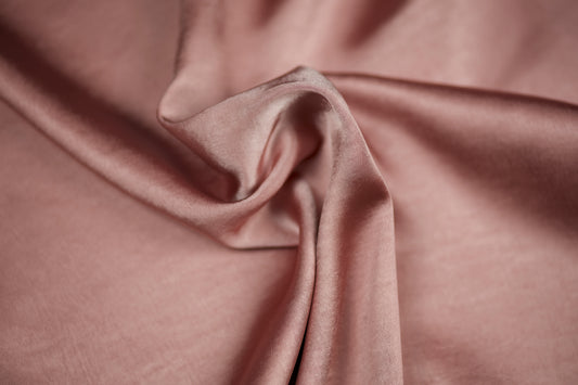 Nahaufnahme eines luxuriösen Satinstoffs in zartem Roséton mit seidigem Schimmer und dekorativer Faltenlegung – ideal für romantische Näharbeiten.